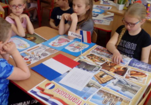 Dzieci siedzące przy stoliku z flagą Francji i obrazkami związanymi z Francją.